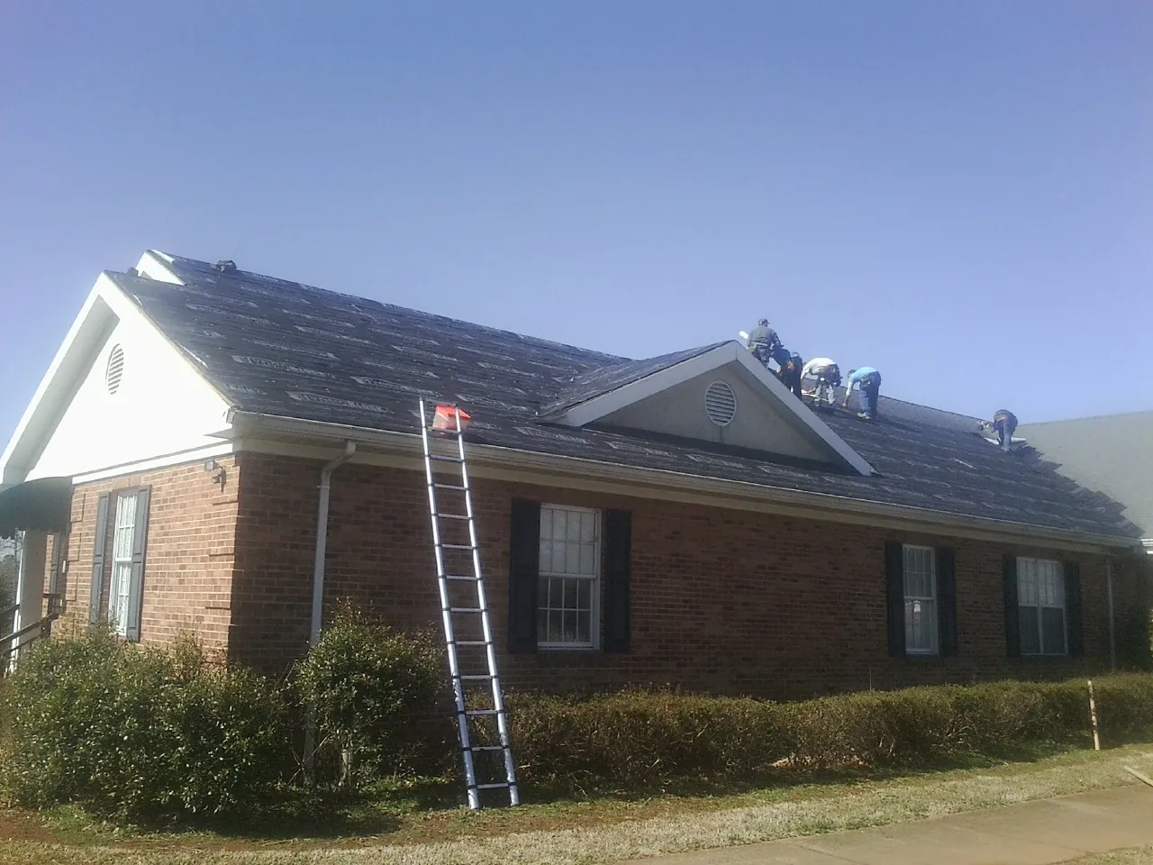 Crew tearing shingles off a brick ranch roof with a ladder set — Emergency Roof Repair work by our crew in Starlight