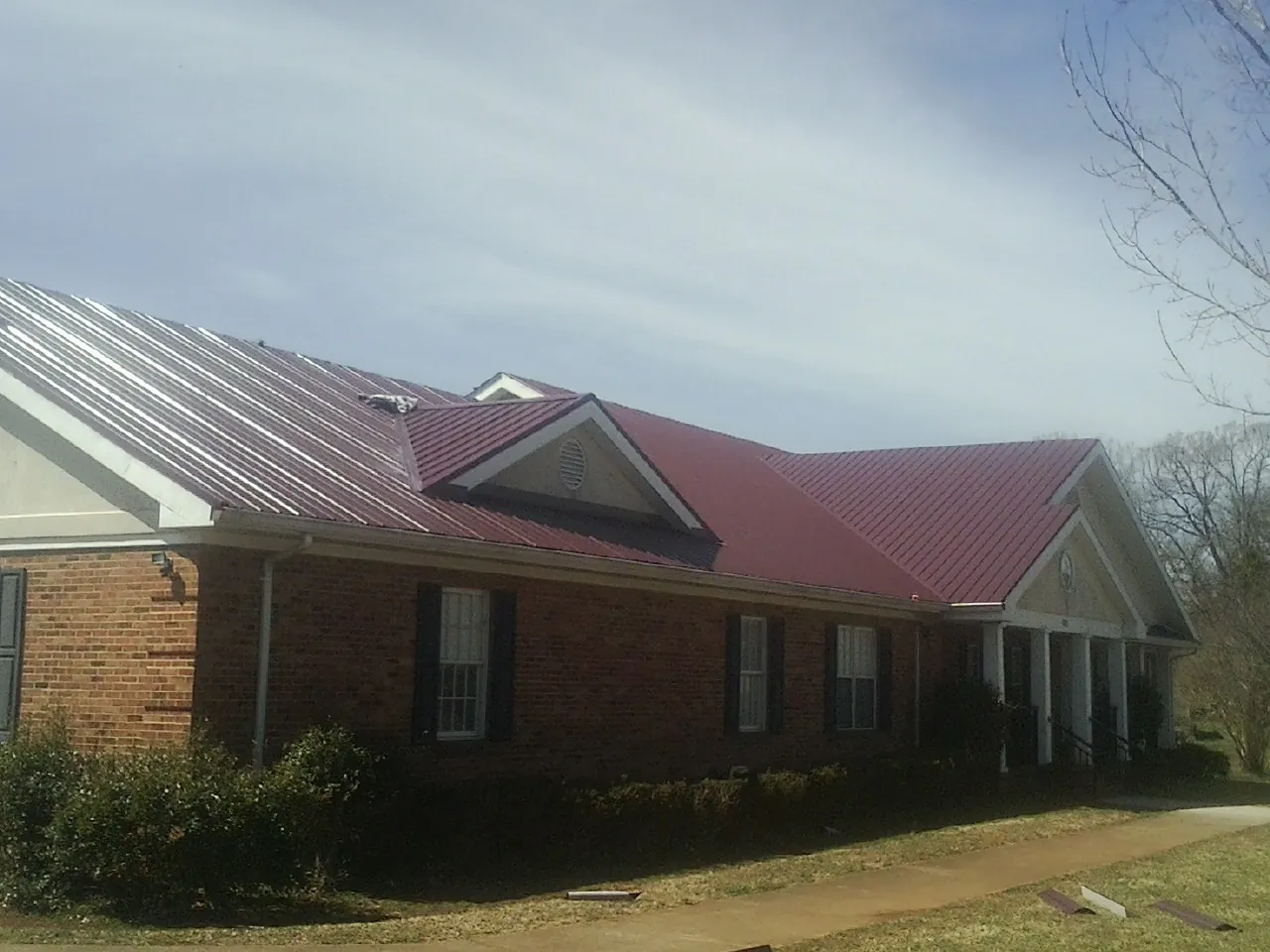 Red metal roof with gabled entries on a long brick building, from a Hail Damage Roof Repair job in Starlight