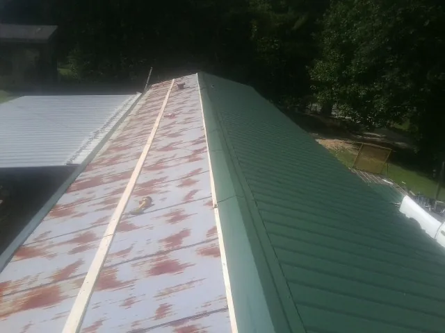 Old rusted panels beside newly installed green metal roofing — Wind Damage Roof Repair by Roofing Brothers in Starlight