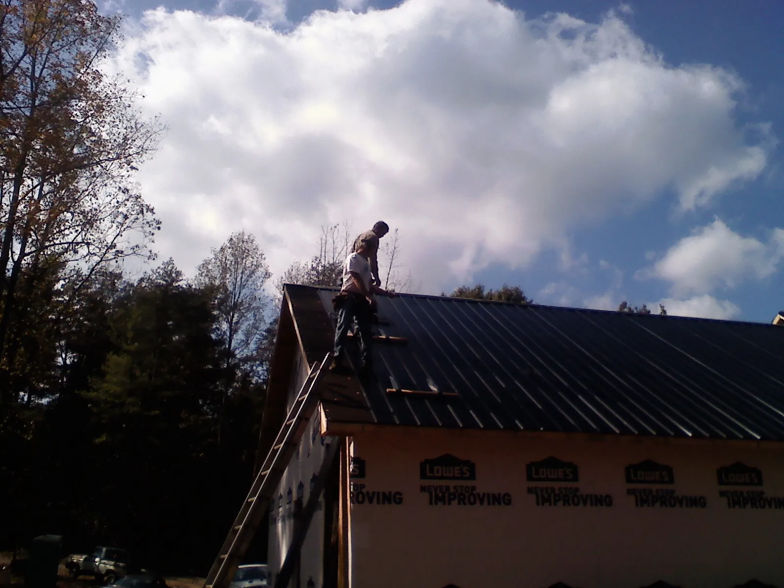 Roofer fastening dark metal panels high against a cloudy sky, from a Roof Inspection job in Starlight